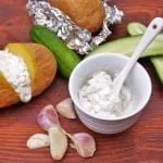 Sos tzatziki w miseczce, ogórki zielone i pieczony ziemniak wypełniony sosem tztaziki