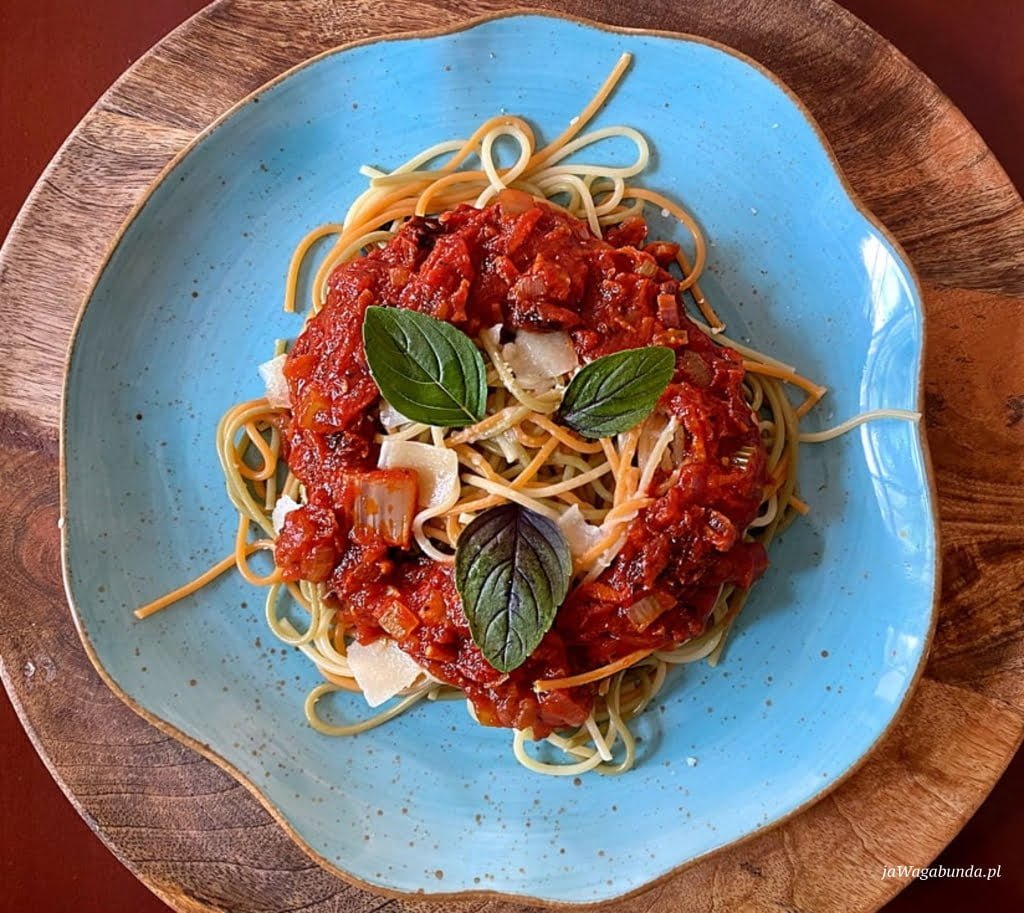makaron spaghetti na niebieskim talerzu polany sosem z pomidorów, listki bazylii na górze