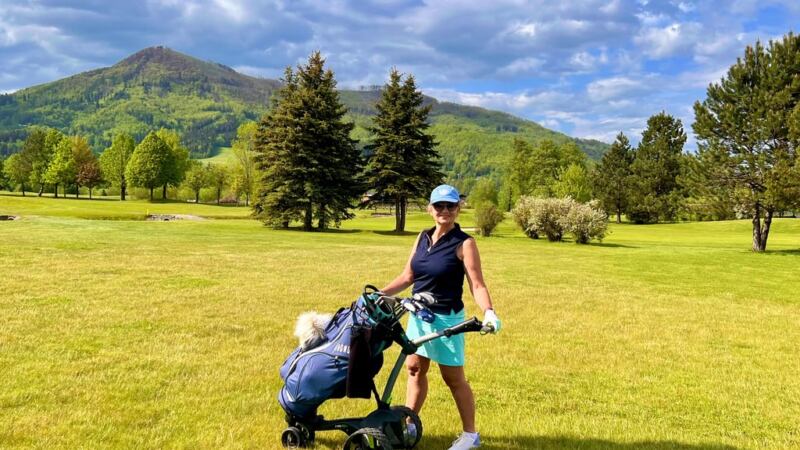 kobieta z wózkiem golfowym na polu golfowym w tle zieleni i gór