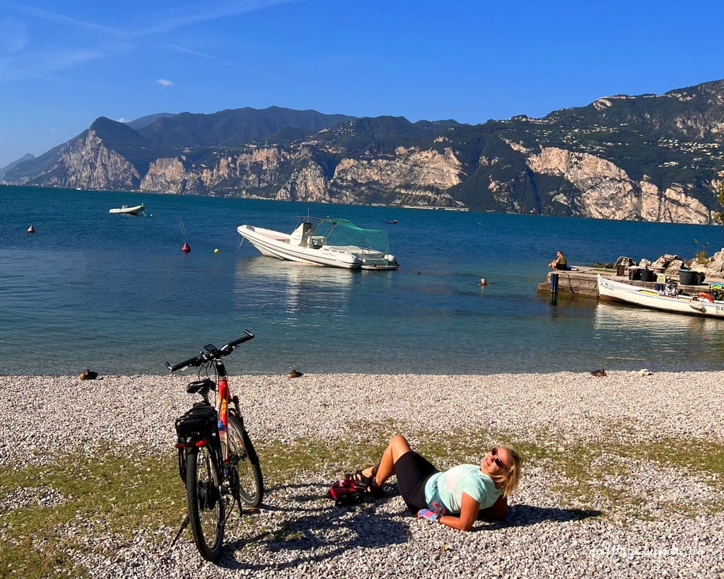 kobieta i rower na plaży nad jeziorem, w tle góry